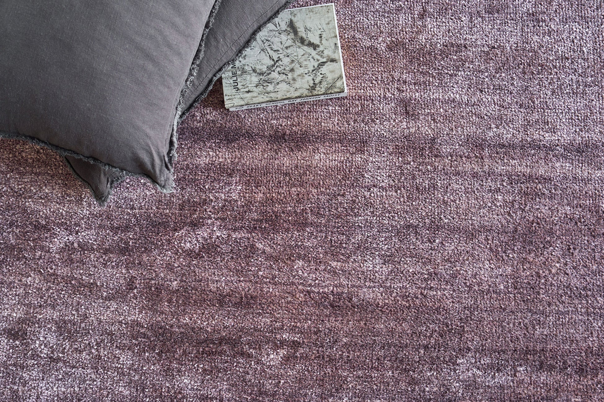 Dusty purple textured area rug with a dark gray pillow resting on its corner; plush, soft pile for contemporary living spaces.