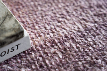 Close-up of mauve-pink hand-knotted rug texture with a white tag peeking from the edge.