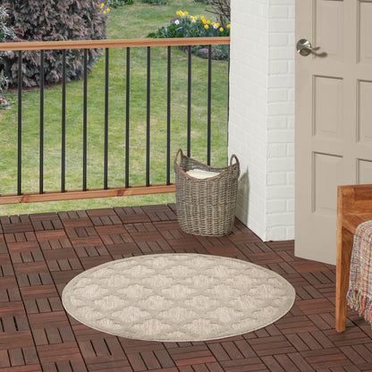 Round beige woven rug on brown wooden deck with a wicker basket beside a white brick wall and door; railing and garden.