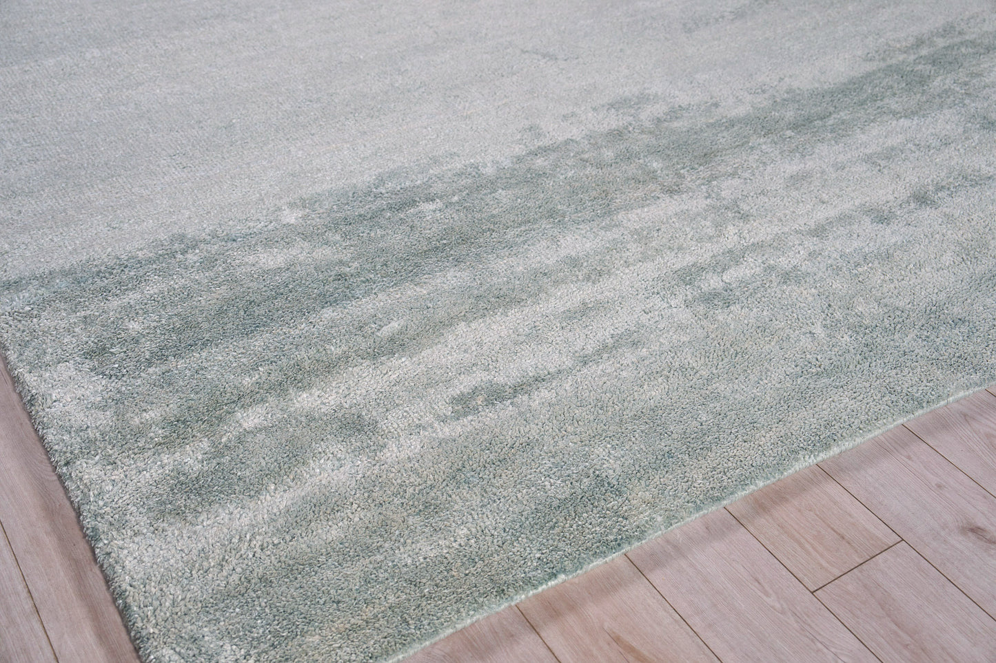 Soft gray-green area rug with subtle color variation and plush pile on light wood flooring.