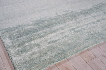 Soft gray-green area rug with subtle color variation and plush pile on light wood flooring.