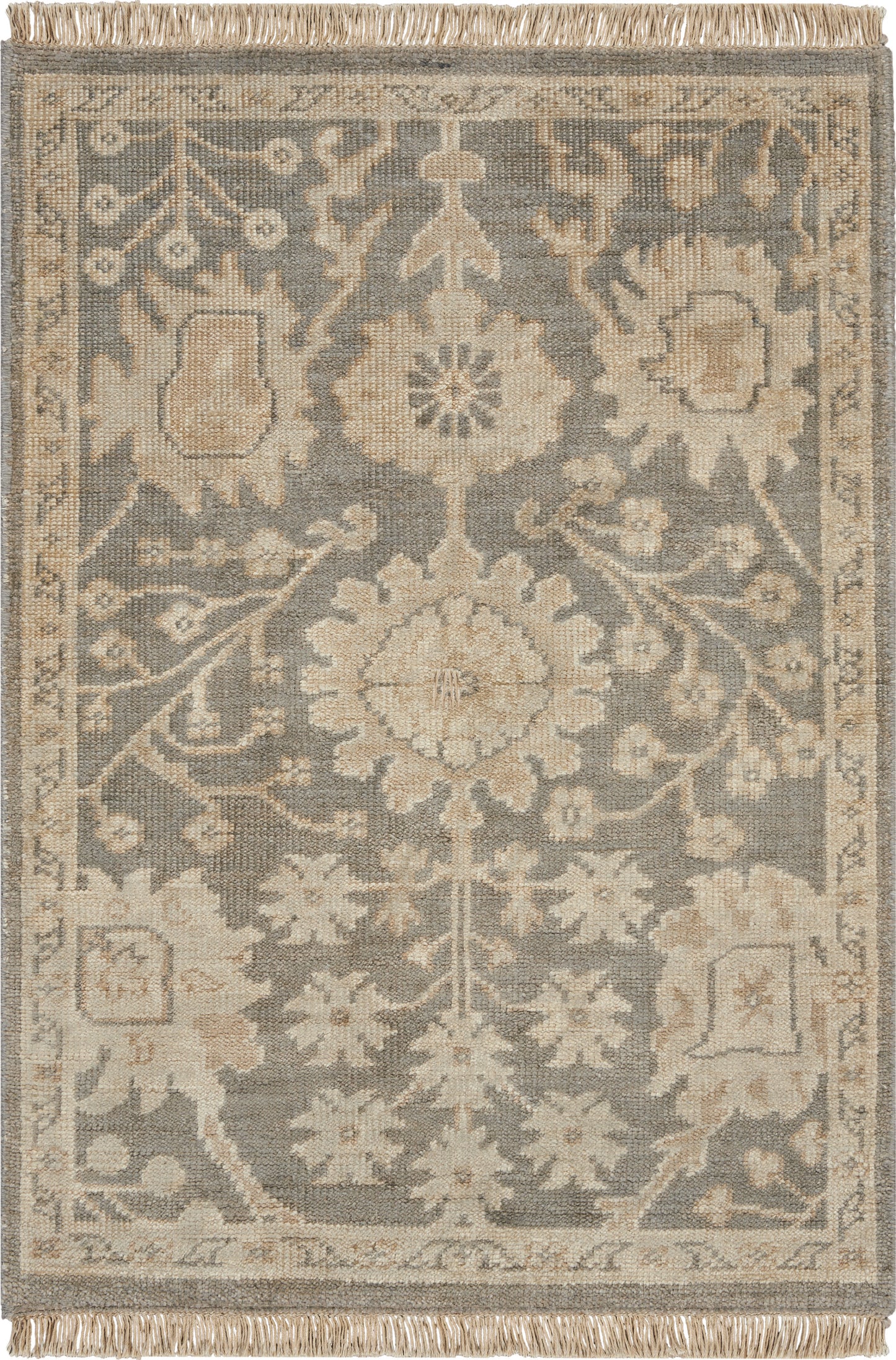 Rectangular area rug in blue-gray and beige with a central floral medallion, ornate border, fringe ends.