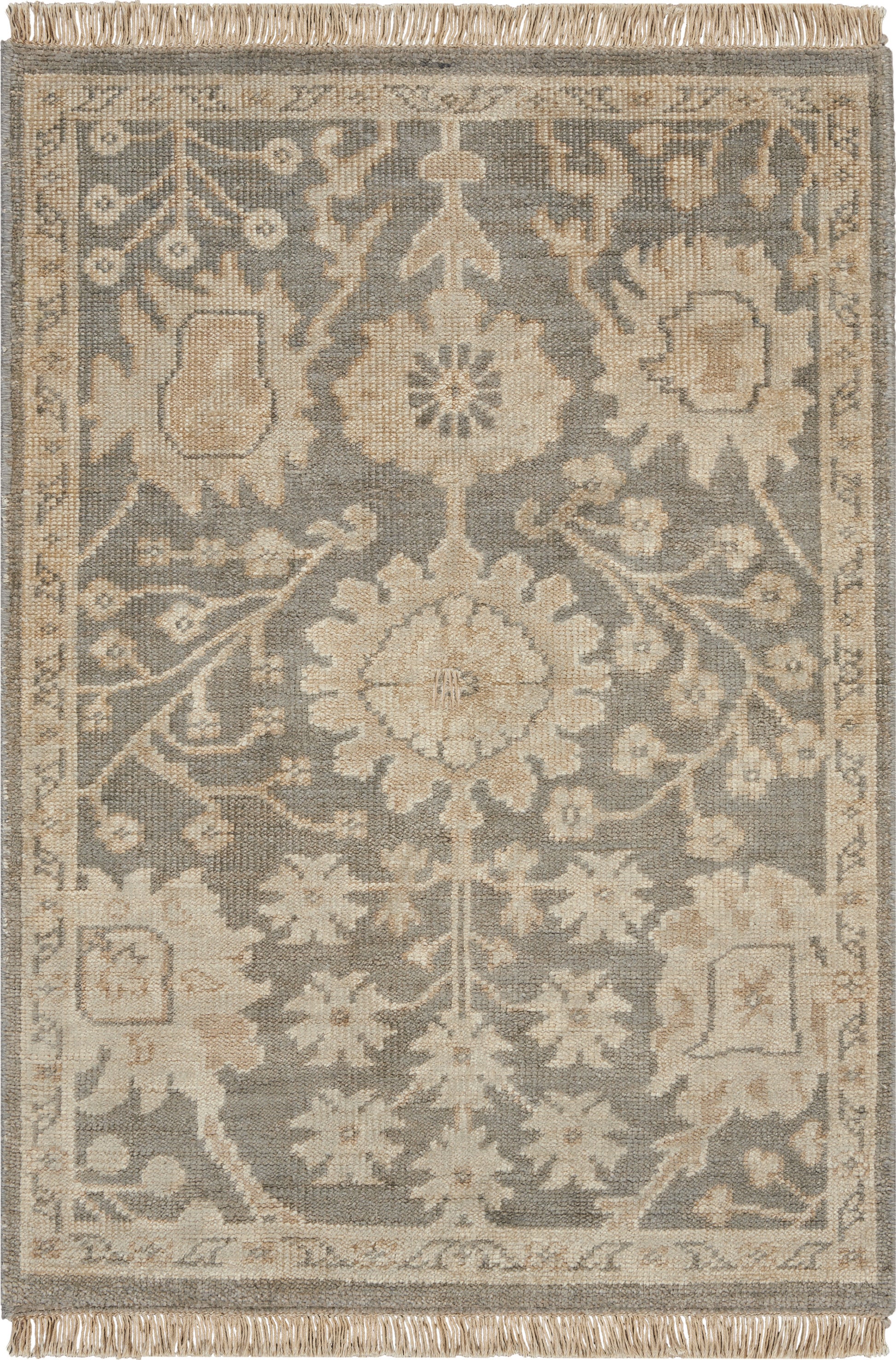 Rectangular area rug in blue-gray and beige with a central floral medallion, ornate border, fringe ends.