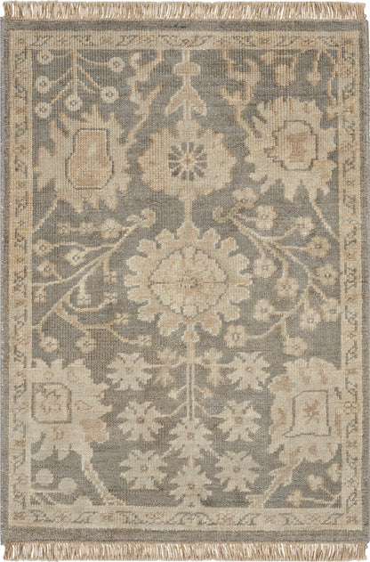 Rectangular area rug in blue-gray and beige with a central floral medallion, ornate border, fringe ends.