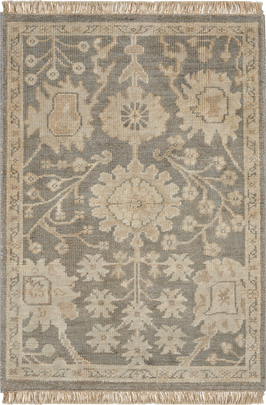 Rectangular area rug in blue-gray and beige with a central floral medallion, ornate border, fringe ends.