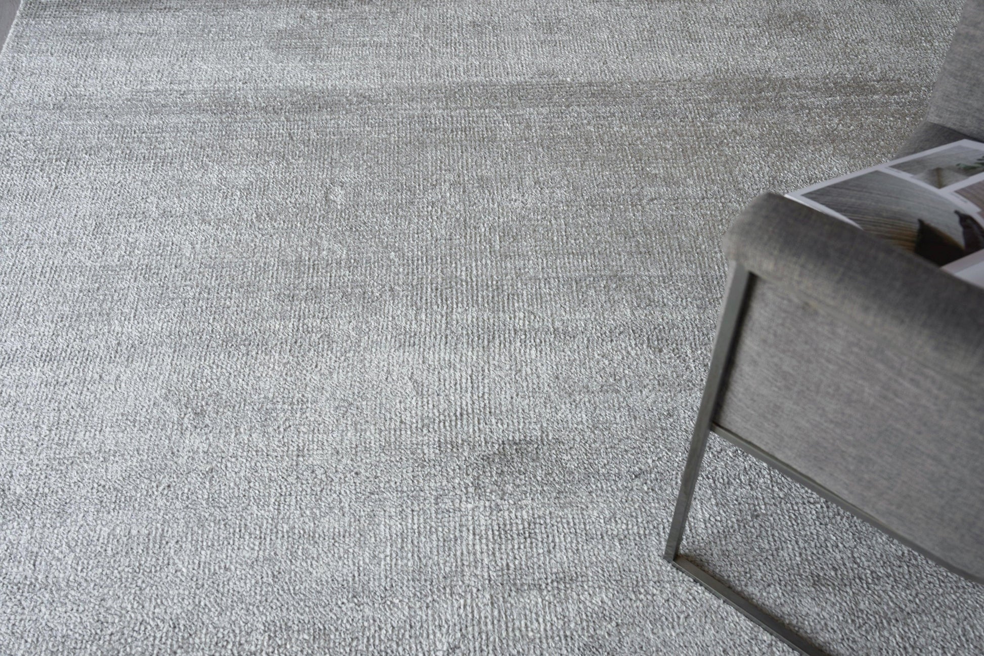 Gray textured area rug with soft weave in a modern living room, near a gray metal-framed chair with a magazine.