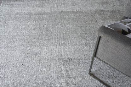 Gray textured area rug with soft weave in a modern living room, near a gray metal-framed chair with a magazine.
