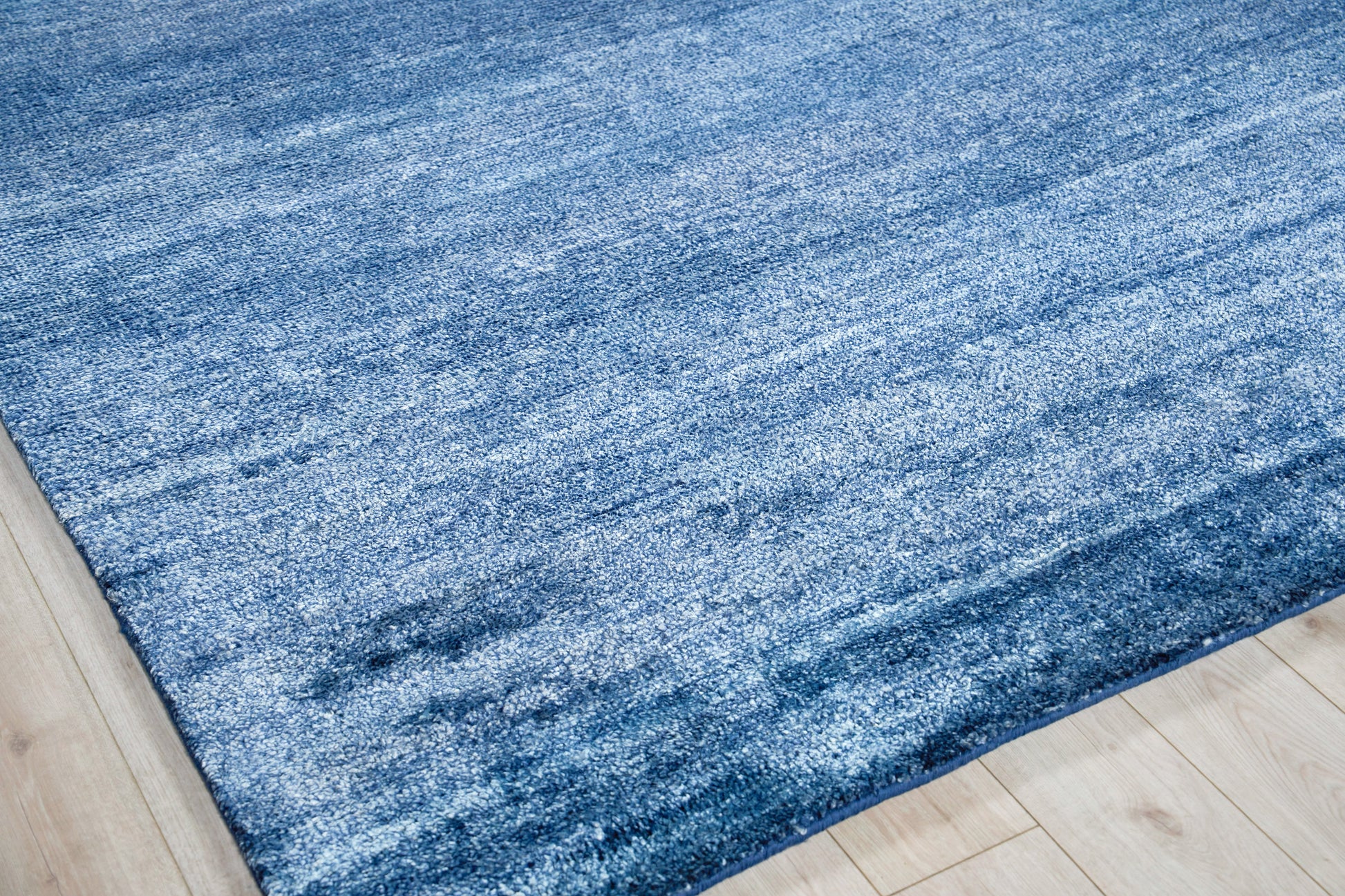 Blue textured area rug with gradient lighter and darker blue tones on a light wood floor.