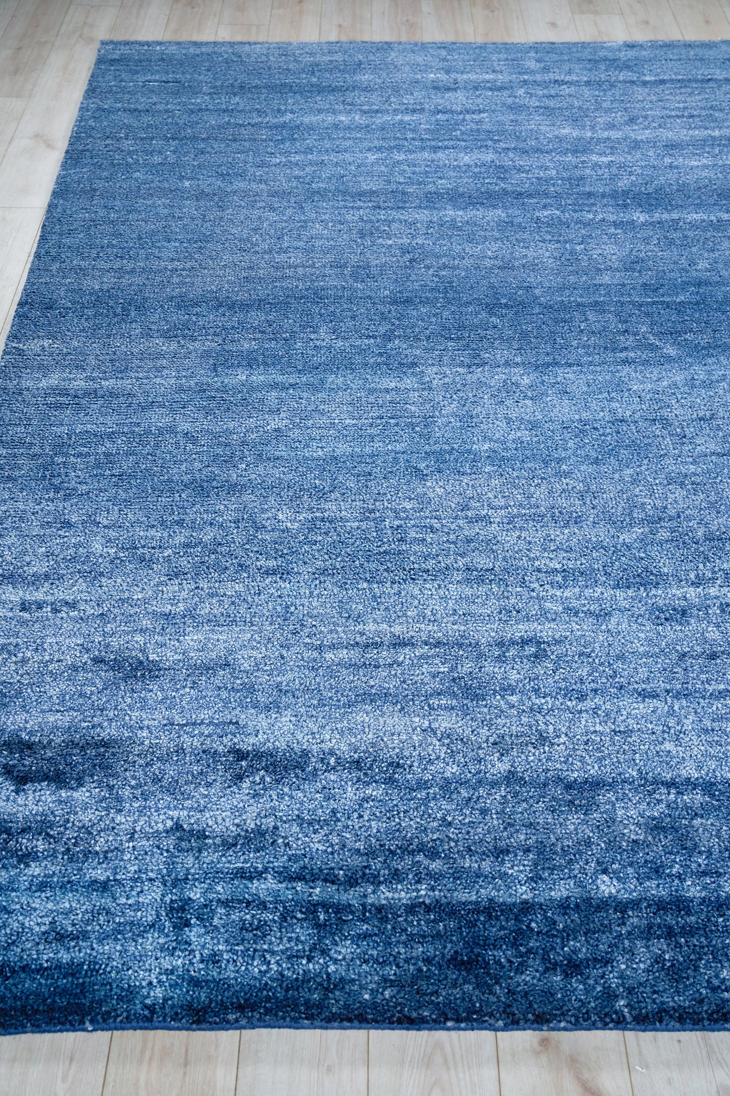 Rectangular blue rug with a subtle gradient and soft plush pile on a light wood floor.