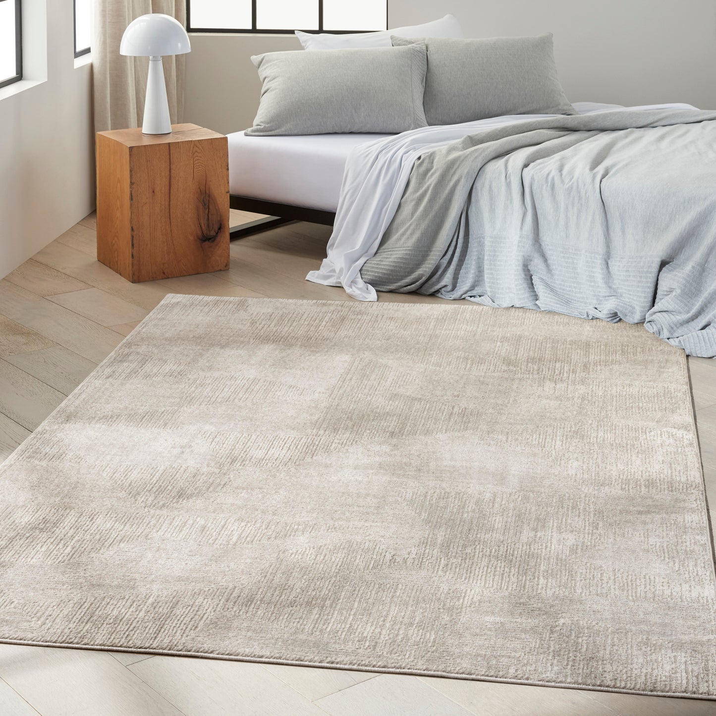 Beige textured area rug in a modern bedroom with light gray bedding, wooden nightstand and white lamp.