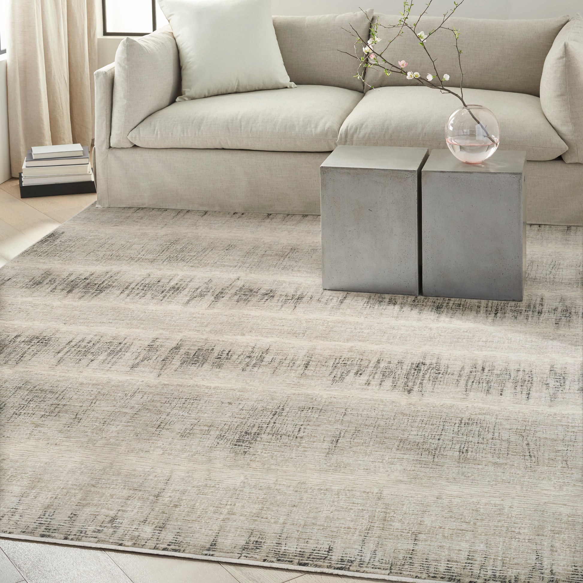 Neutral living room: beige sofa, light gray distressed rug, two concrete cube tables with a glass vase of flowering branches.