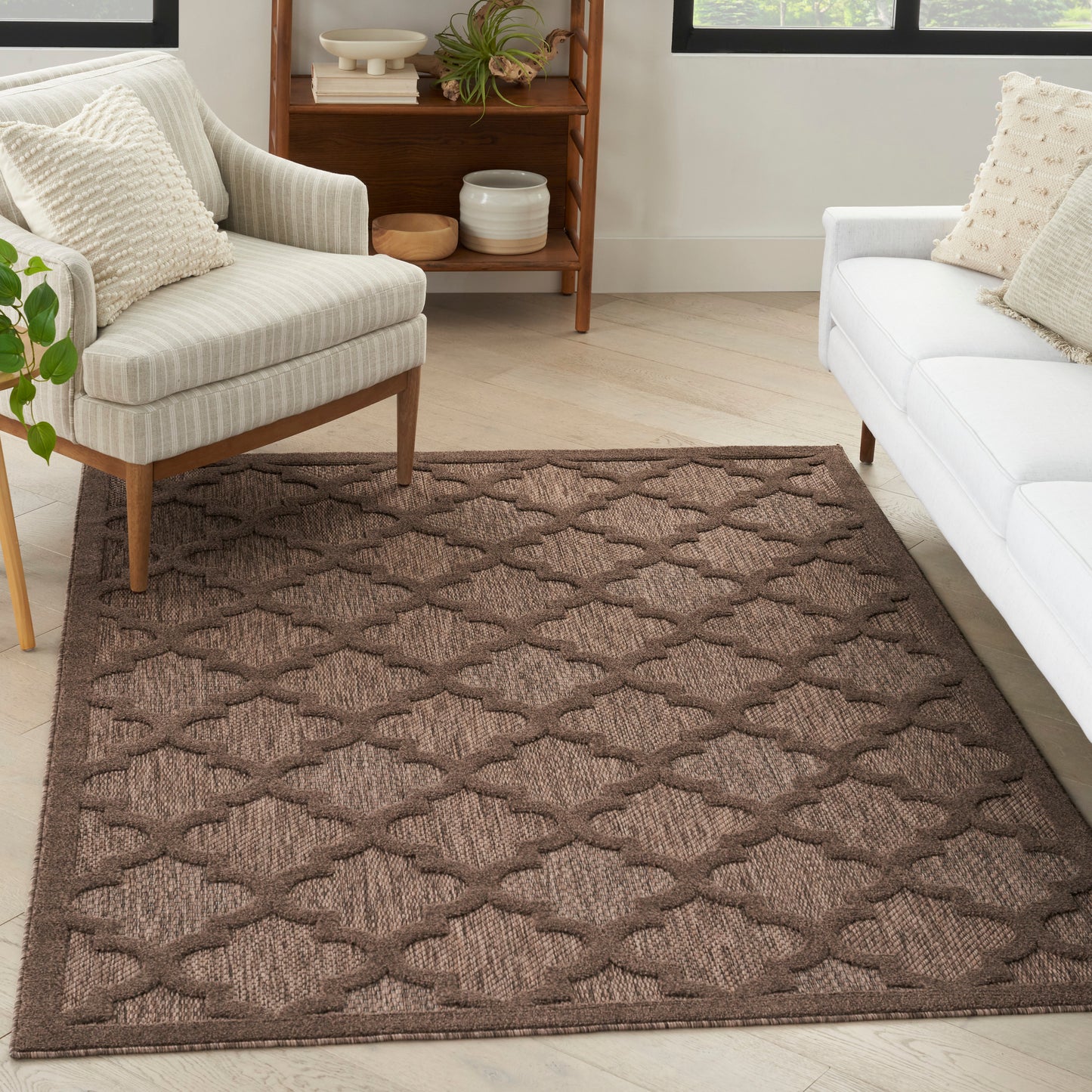 Brown geometric trellis rug in a cozy living room with cream armchair, white sofa, and light wood floors.