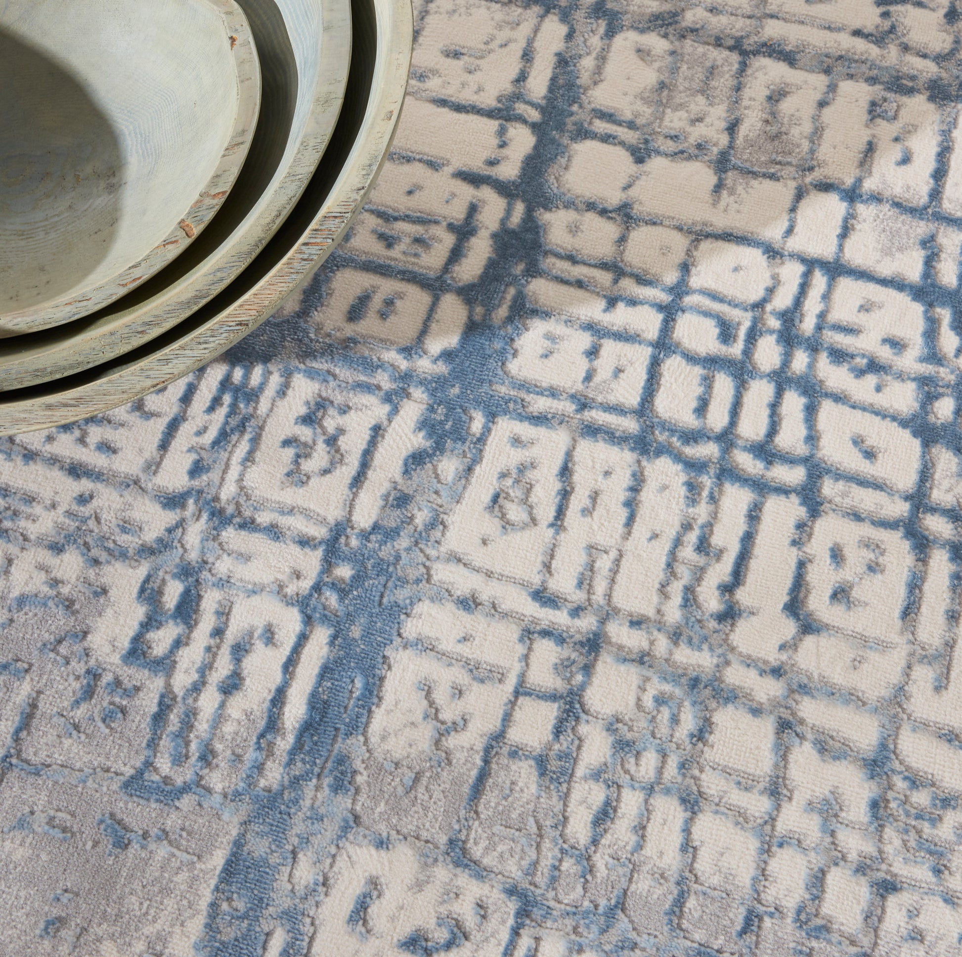 Stacked beige ceramic bowls on a blue geometric patterned rug.