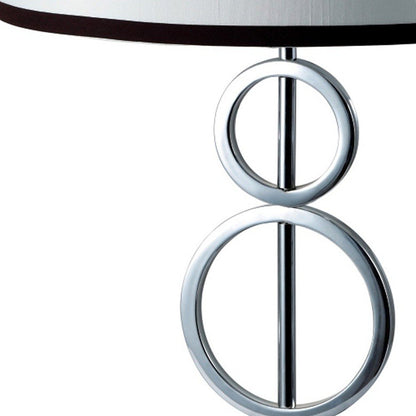 Chrome bedside geo table lamp with stacked circular rings on a vertical rod and a white and black trim drum shade.