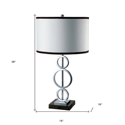 Silver metal bedside geo table lamp with white drum shade and black trim, stacked circular ring accents.