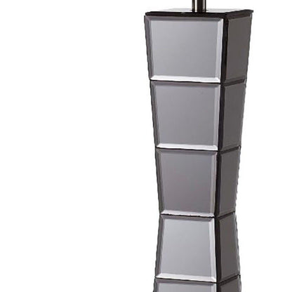 Table lamp with a black glass tower and a beige fabric shade.