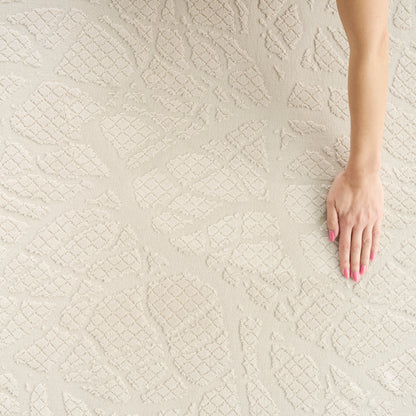 Beige textured rug with raised geometric diamond motifs; hand with pink nail polish resting on it.