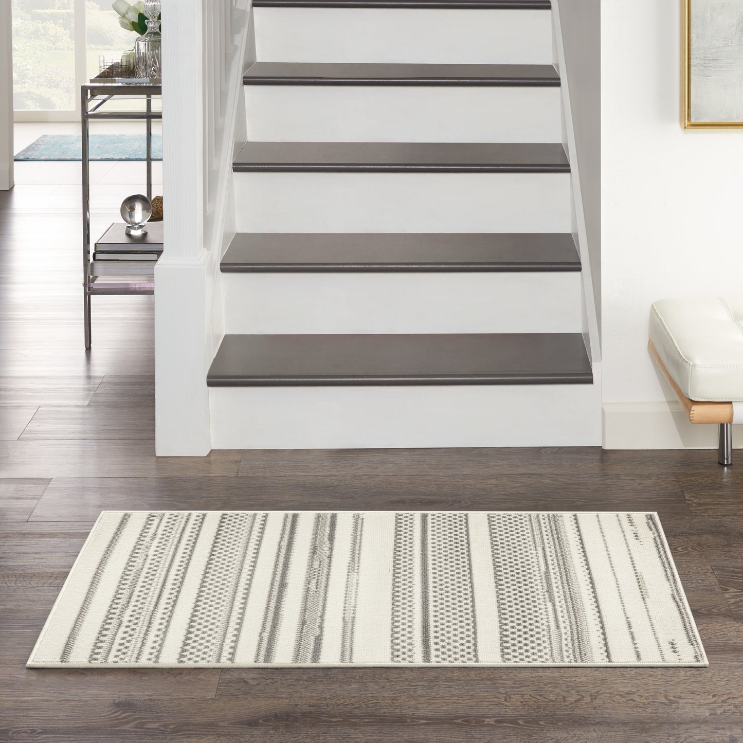 Rectangular cream area rug with grey geometric stripes on dark hardwood floor in front of a modern white staircase.