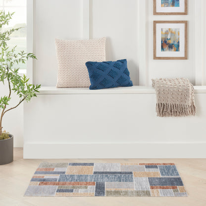 White built-in bench with beige knit pillow, blue cushion, beige fringe throw; abstract wall art, potted plant, patchwork rug.