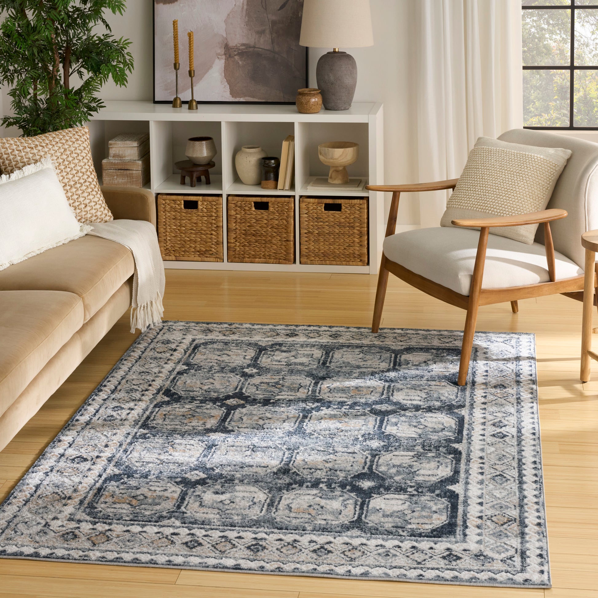 Blue distressed geometric area rug with ivory border on light wood floor in a cozy living room.