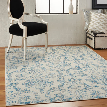 Cream and blue damask area rug under a vintage white carved chair with black cushion in a bright room.
