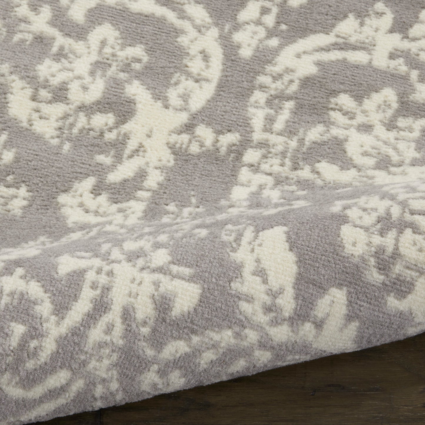 Close-up of gray rug with cream damask floral pattern and soft textured pile on a wooden floor.