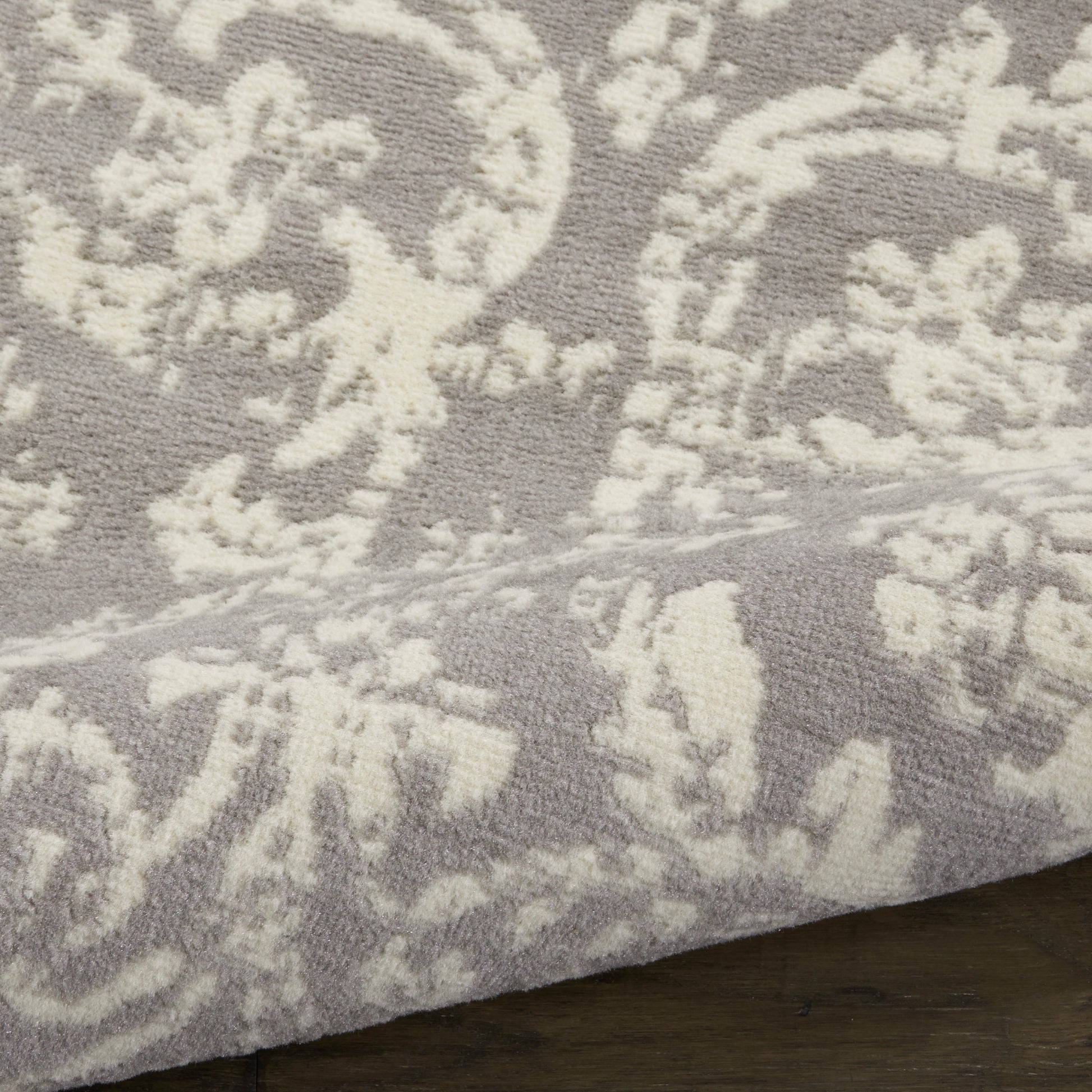 Close-up of gray rug with cream damask floral pattern and soft textured pile on a wooden floor.