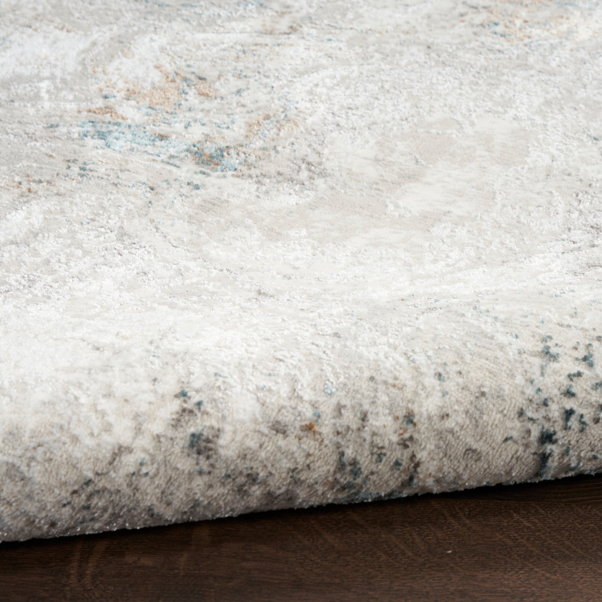 Close-up of a light gray-beige rug edge on a dark wood floor with subtle blue accents.