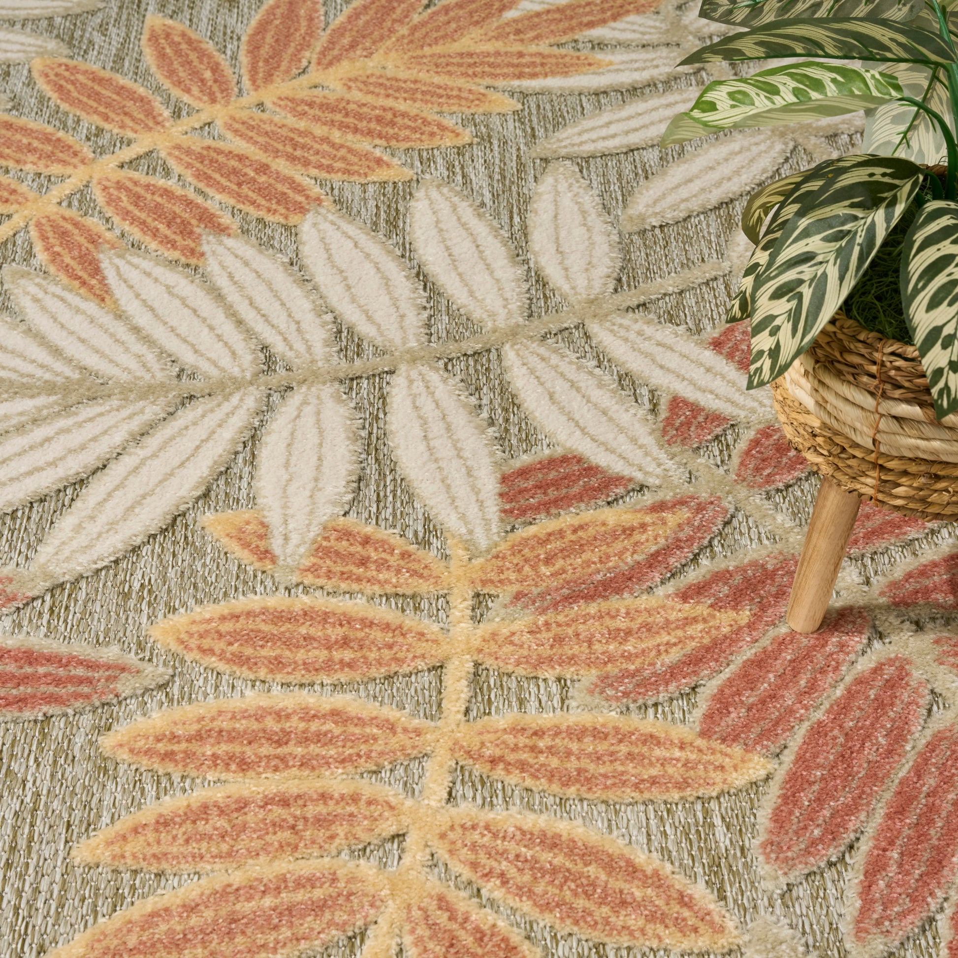 Boho rug with orange & cream leaf pattern on gray; potted plant in woven basket nearby.