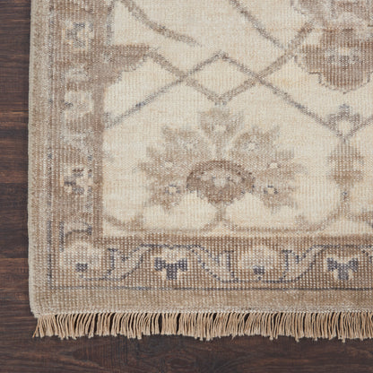 Beige oriental rug corner with fringe on dark wood floor; blue-grey border and ornate floral, geometric medallion pattern.