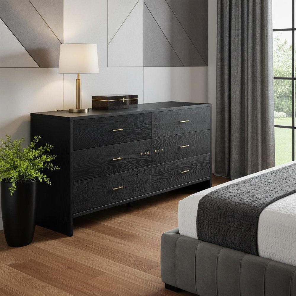 Dark wood six-drawer dresser with gold handles, lamp on top and potted plant in a modern gray-toned bedroom.