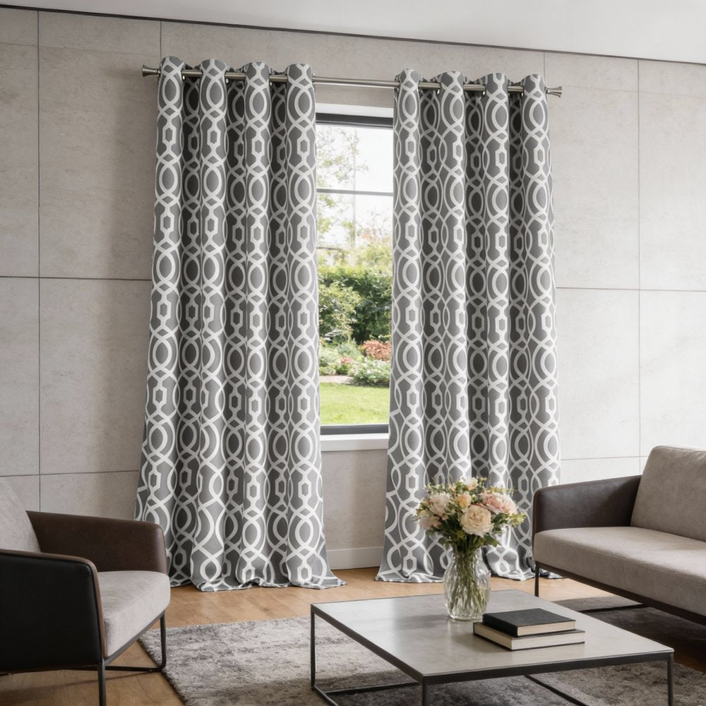 Grey and white geometric patterned curtains in a modern living room with neutral sofa and glass coffee table.