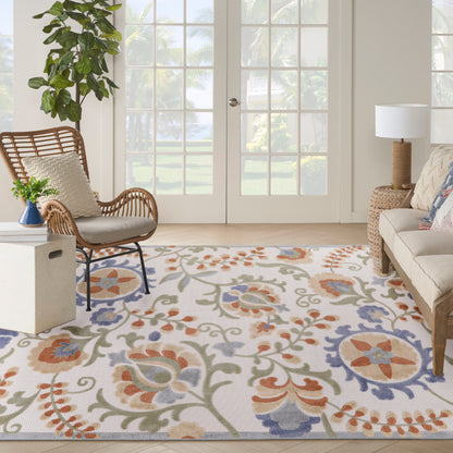 Bright living room with a colorful floral area rug, a rattan chair, beige sofa, potted plant, and glass French doors.