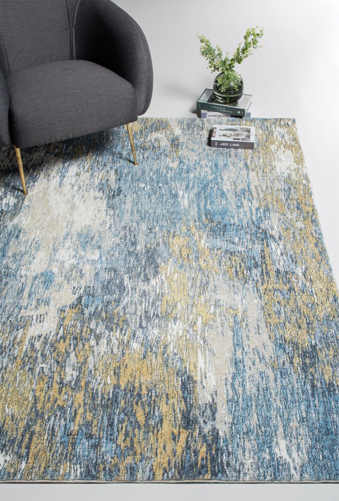 Abstract blue, gray, and tan area rug under a dark gray armchair with gold legs; small side table with plant.