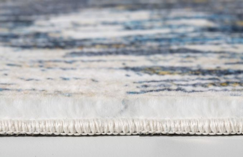 Close-up of a blue and gold abstract rug with a white fringe along the edge, modern decorative floor covering.