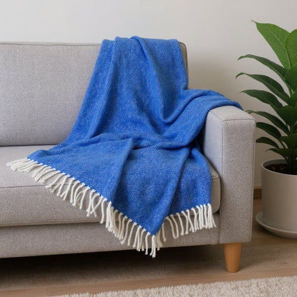 Bright blue throw blanket with white fringe draped over a light gray sofa.