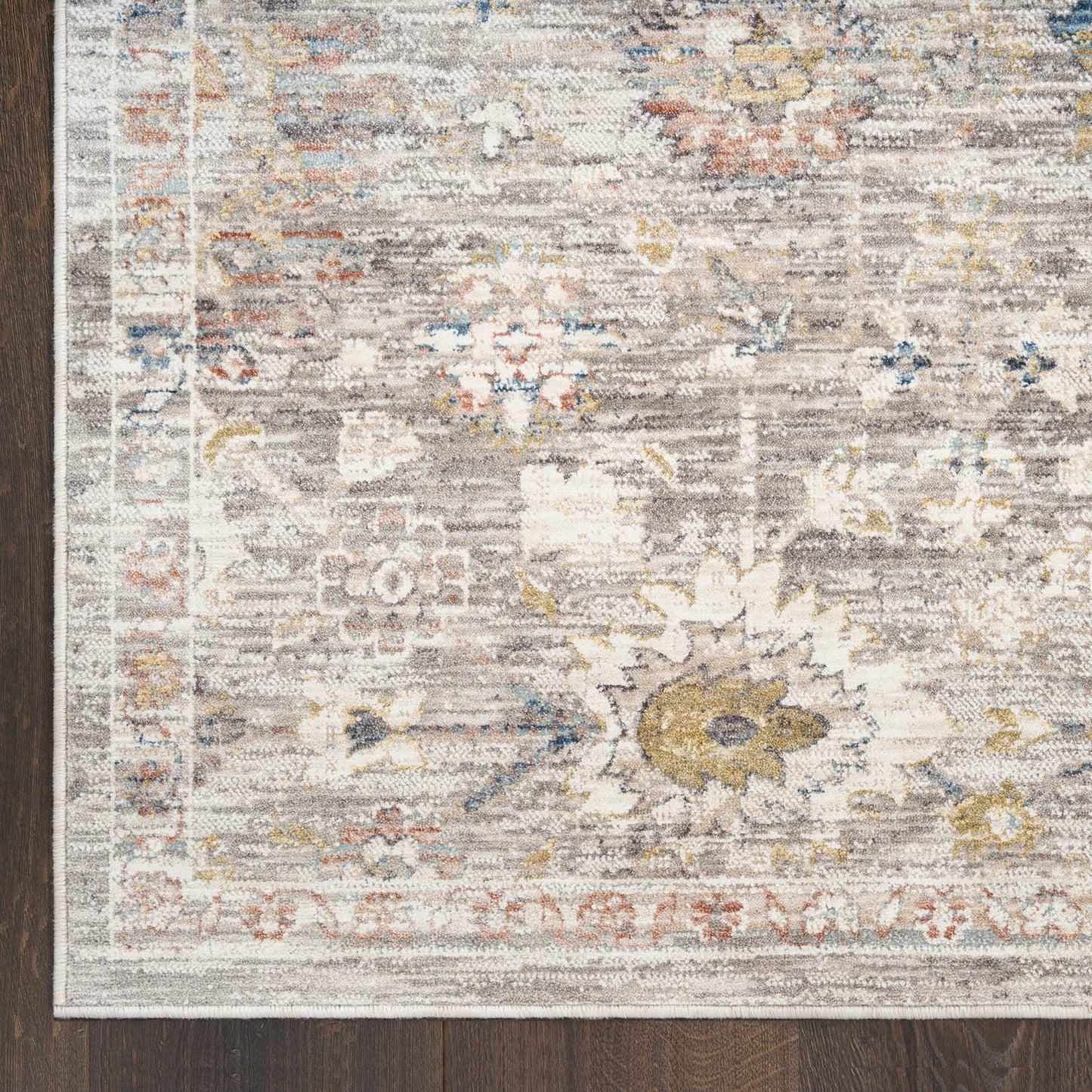 Rectangular distressed traditional rug with cream, gray, blue and gold floral motifs and border on dark wood floor.