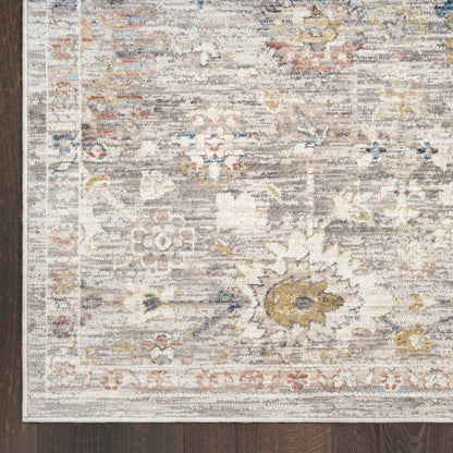 Rectangular distressed traditional rug with cream, gray, blue and gold floral motifs and border on dark wood floor.