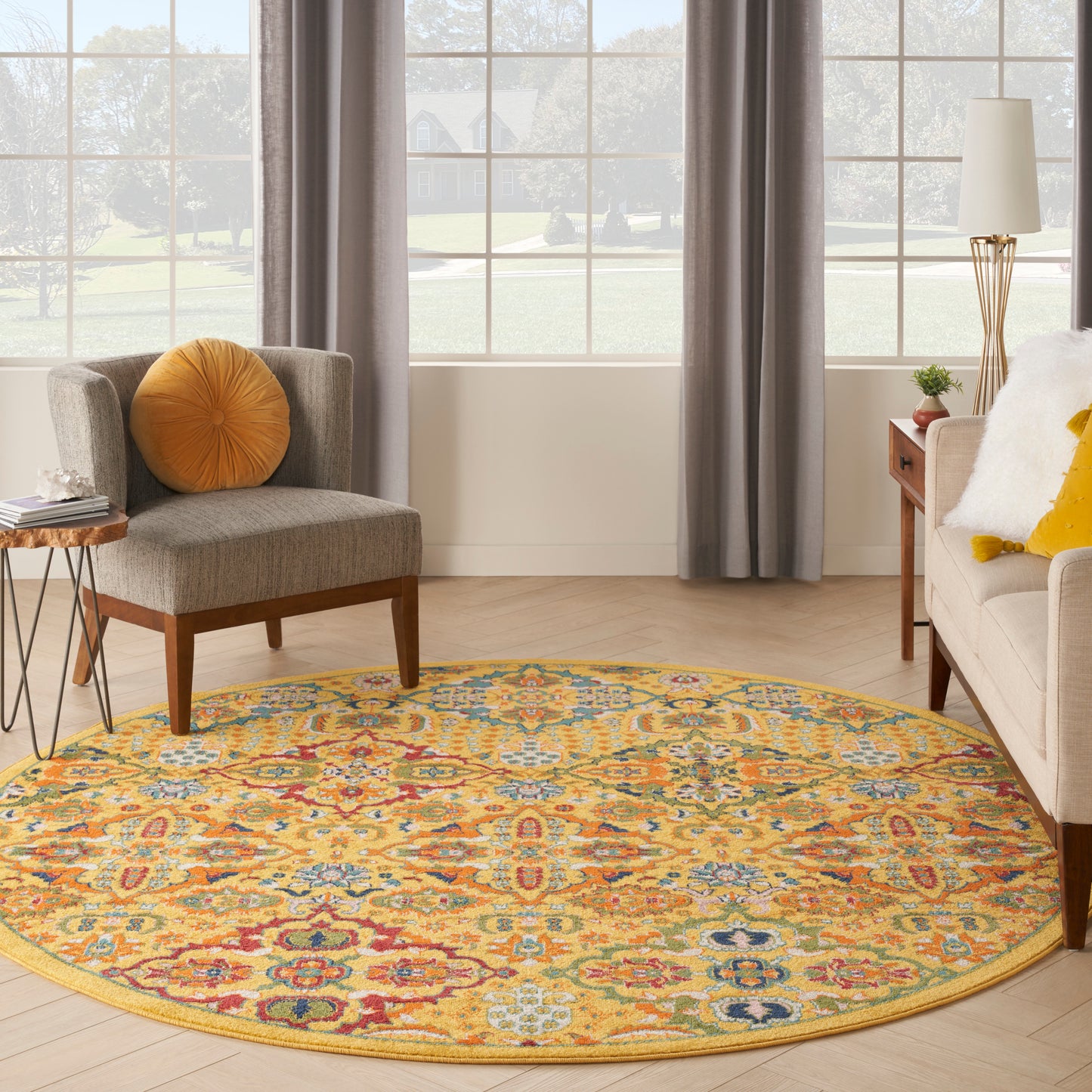 Round colorful rug with yellow border in a living room; gray chair with orange pillow and beige sofa with yellow cushions.