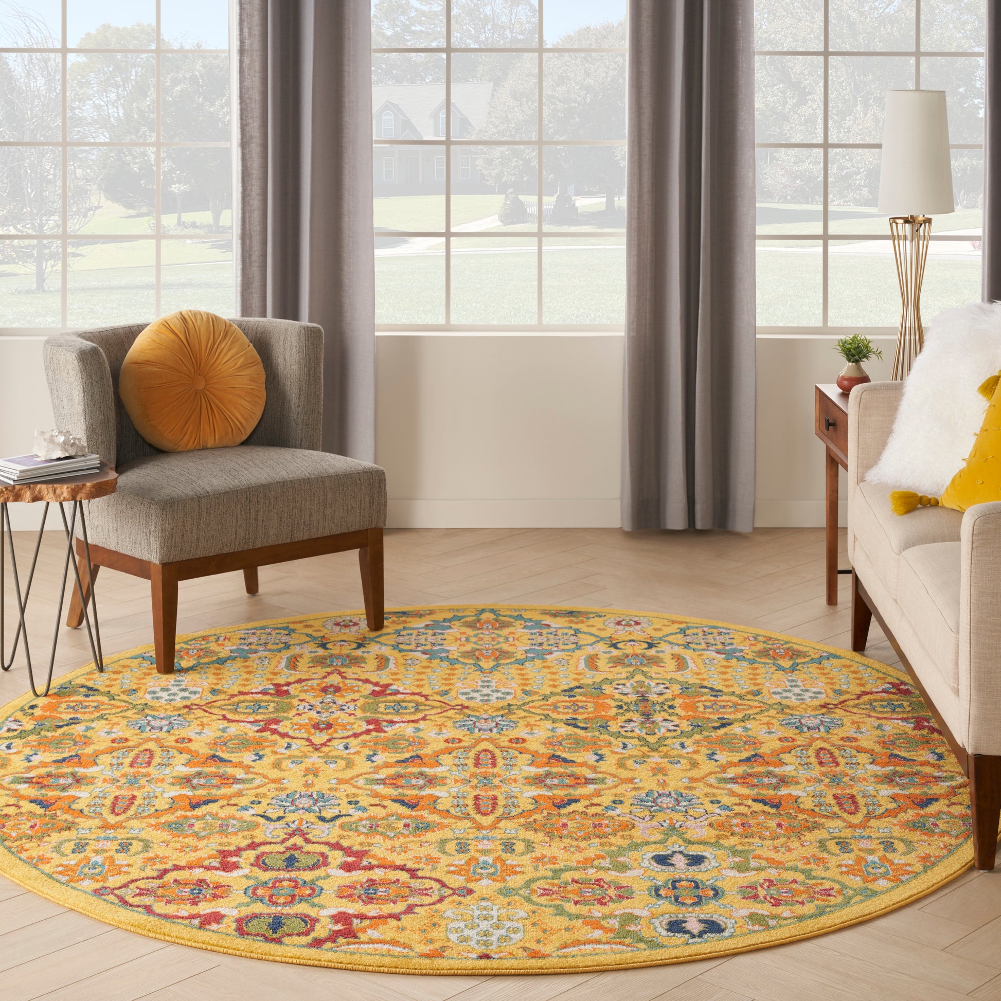 Round colorful rug with yellow border in a living room; gray chair with orange pillow and beige sofa with yellow cushions.