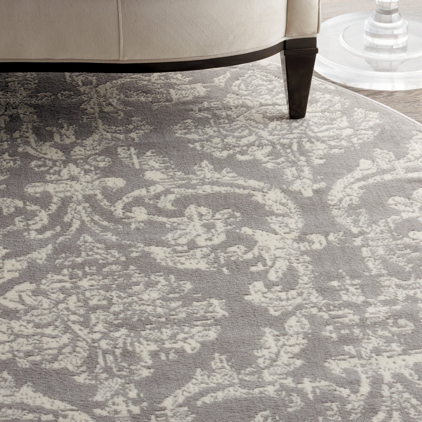 Gray and ivory damask patterned area rug under a beige sofa with a dark wood leg.