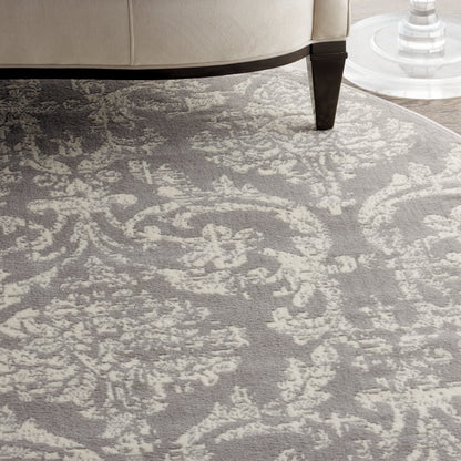 Gray and ivory damask patterned area rug under a beige sofa with a dark wood leg.