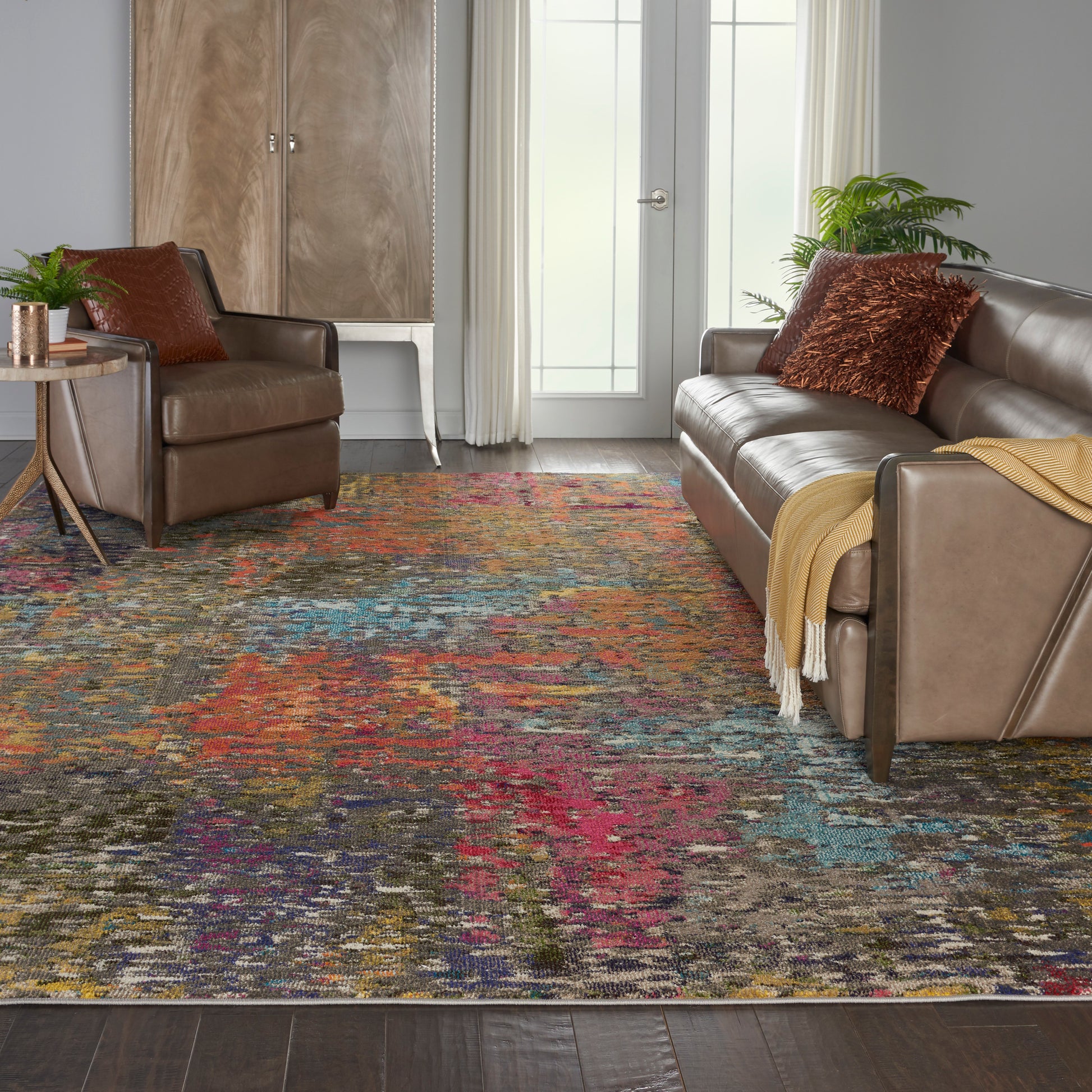 Vibrant multicolor distressed area rug over dark wood floor with brown leather sofa and chair, throw blanket.