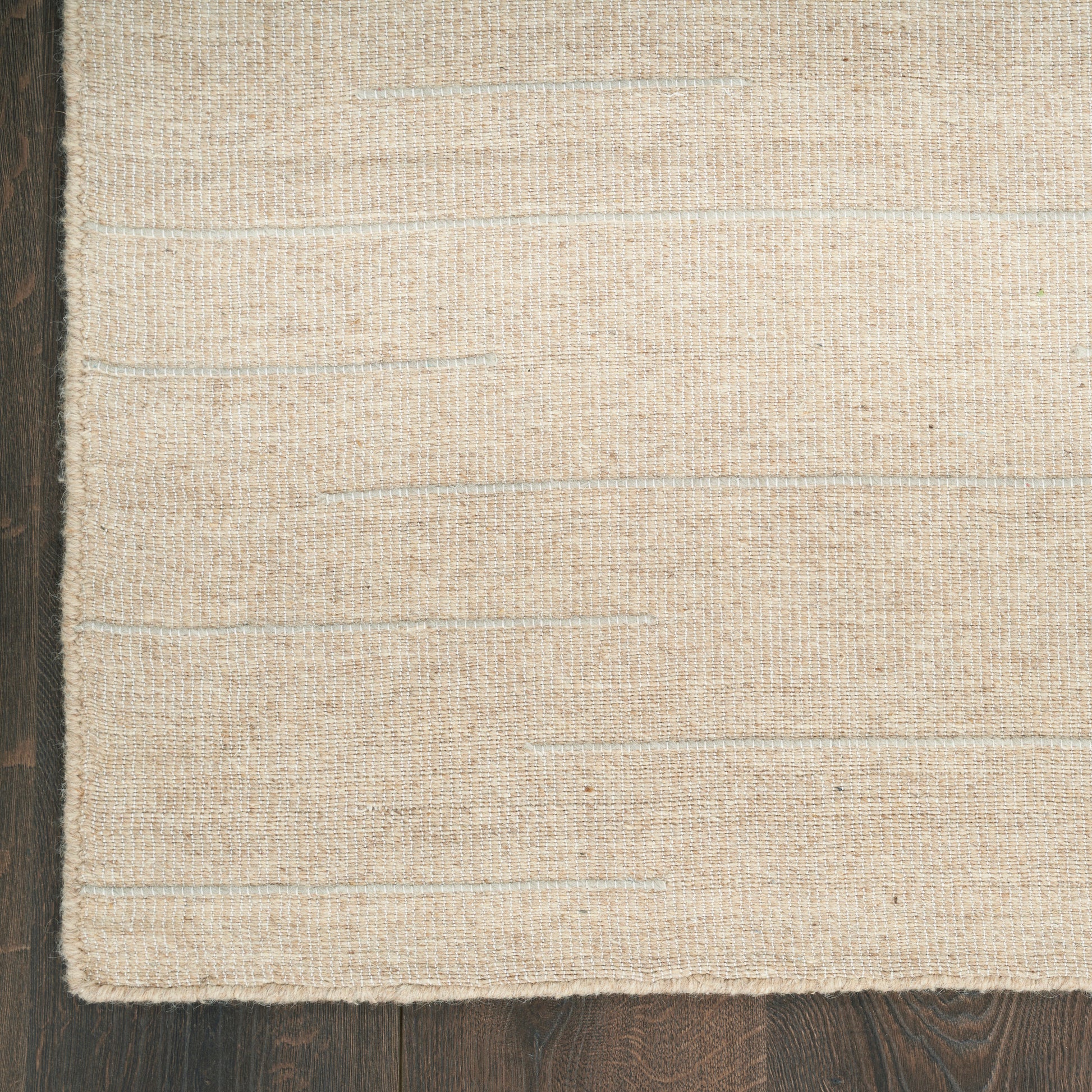 Beige natural-fiber flat-weave rug with subtle horizontal texture on dark hardwood floor