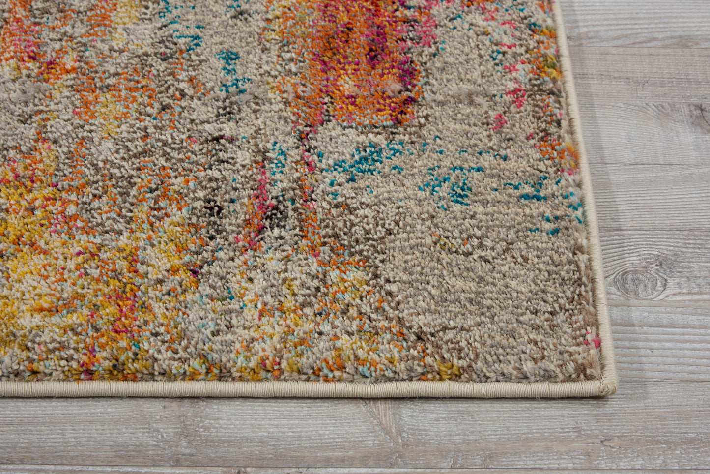 Rectangular tufted area rug with beige base and vibrant abstract pattern in orange, pink, blue and yellow on a light wood floor.