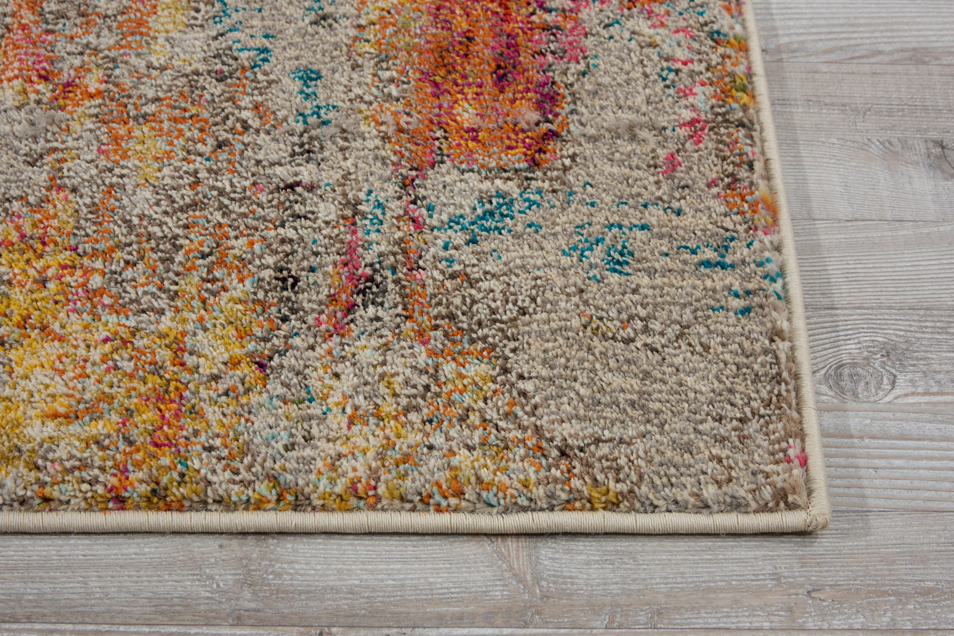 Rectangular tufted area rug with beige base and vibrant abstract pattern in orange, pink, blue and yellow on a light wood floor.
