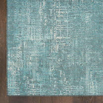 Teal blue abstract-pattern area rug with light geometric lines on dark wood floor.