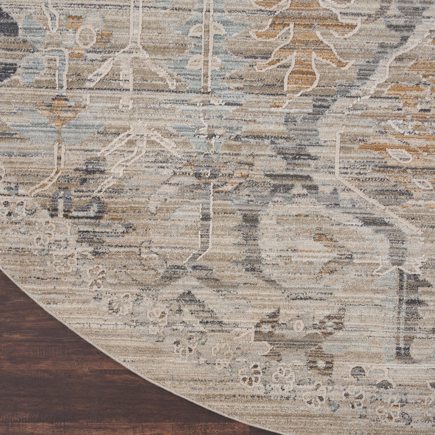 Distressed vintage-style round rug with muted beige, ivory, gray and blue floral motifs; wood floor edge visible.