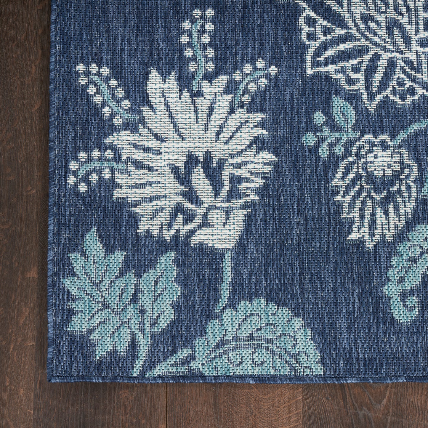 Navy blue woven rug with large white floral and teal leaves pattern on dark wood floor.
