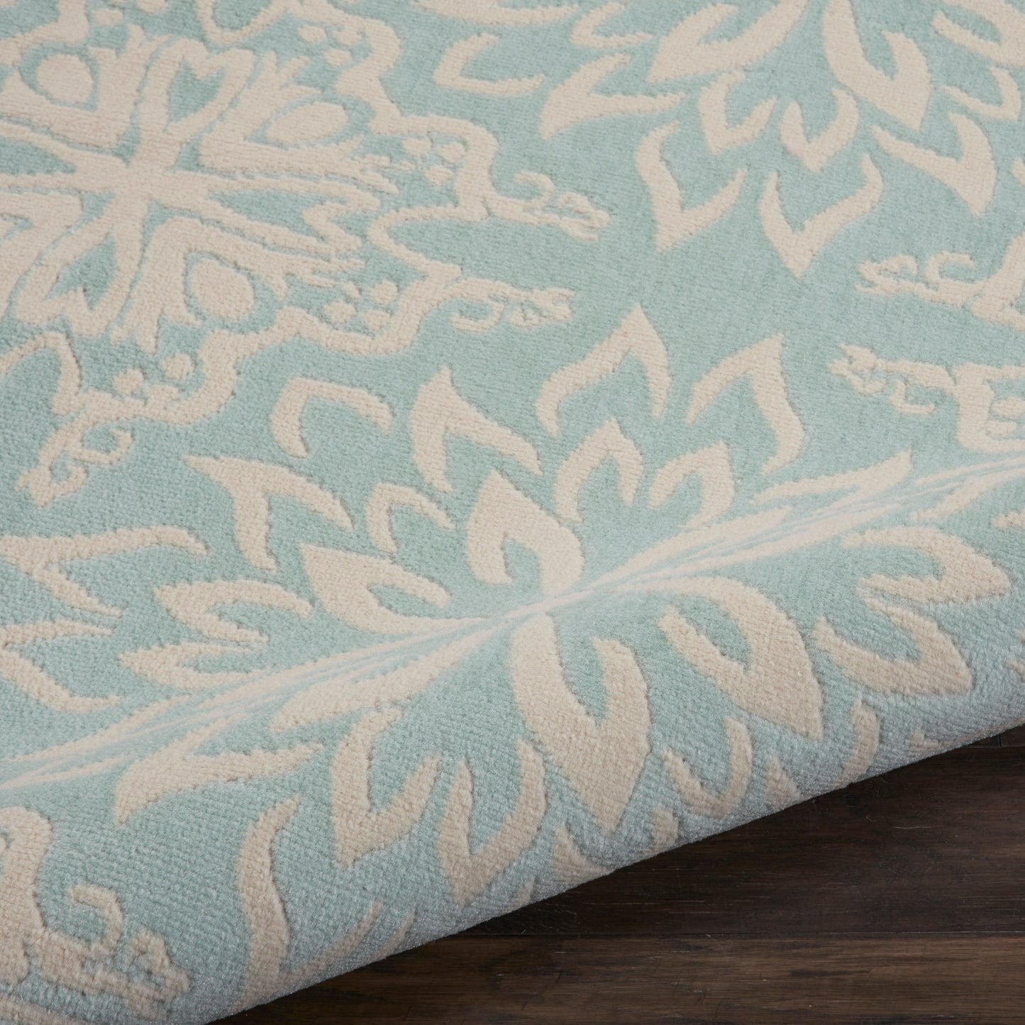 Light blue textured rug with white damask floral pattern draped over a dark wooden surface, 8' x 10'.